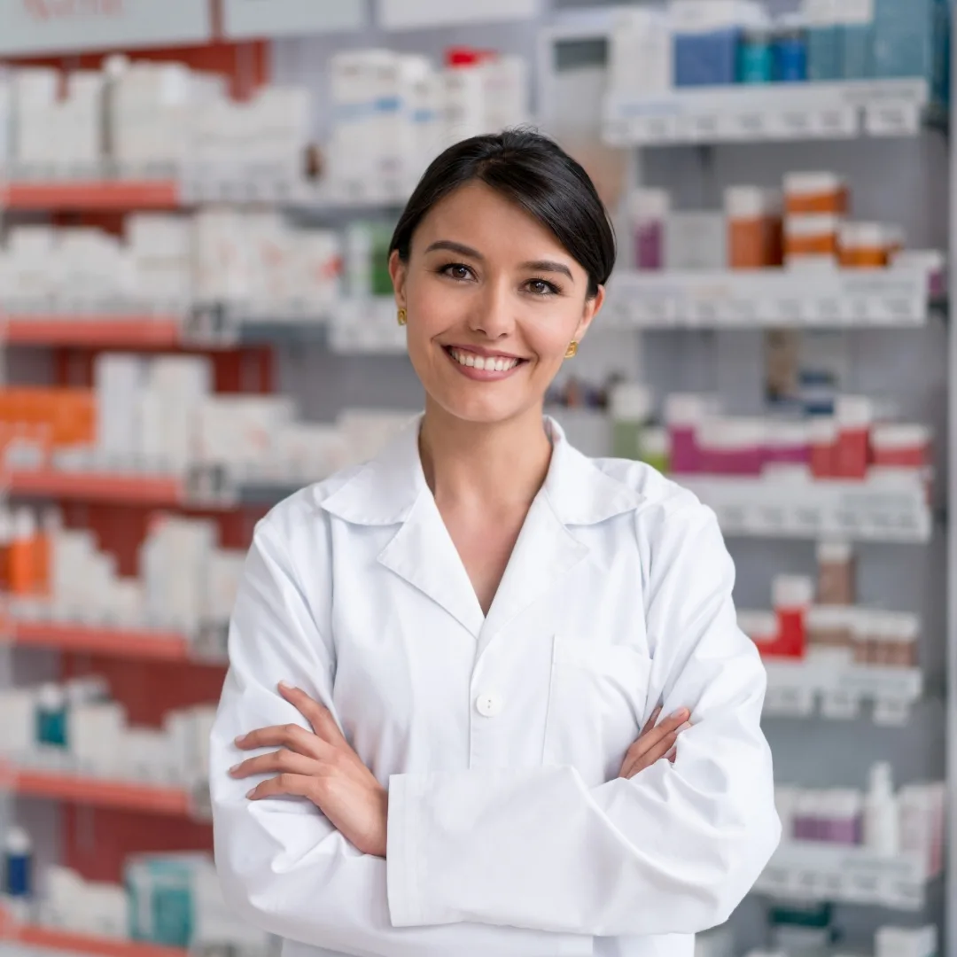Smiling pharmacist in a white coat in front of the medicine shelves